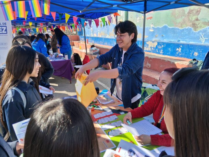 Feria Bienestar, Escuela Chorrillos. Jóvenes reciben Pasaporte de Emociones en stand de salud mental y diversidad, con banderines arcoíris.