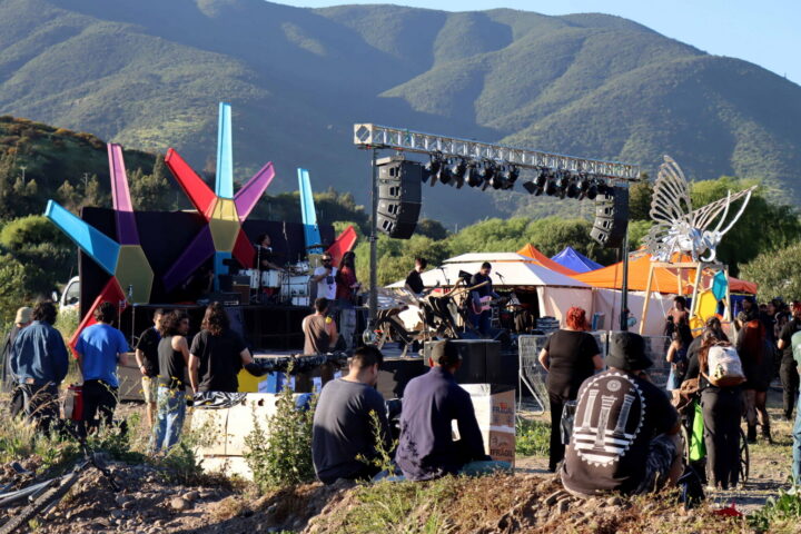 Vista del escenario del festival Rock en Río Aconcagua, con artistas actuando y un público reunido frente al escenario en un entorno natural montañoso.