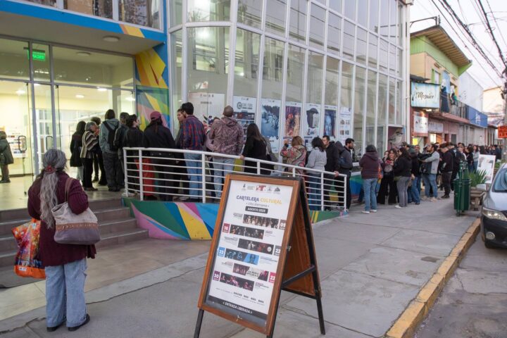 Una fila de personas espera en la entrada del Centro Cultural Gabriela Mistral, con carteles de programación en la entrada.