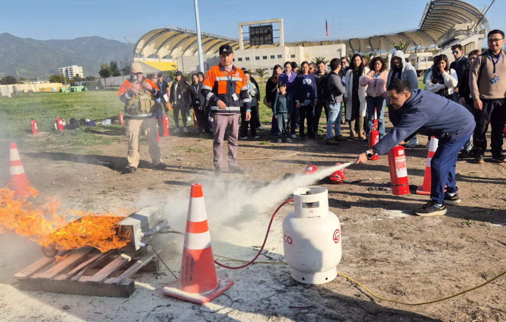 Funcionario de SaludQuillota usa extintor en simulador de fuego. Capacitación práctica en emergencias y seguridad en centros de salud.