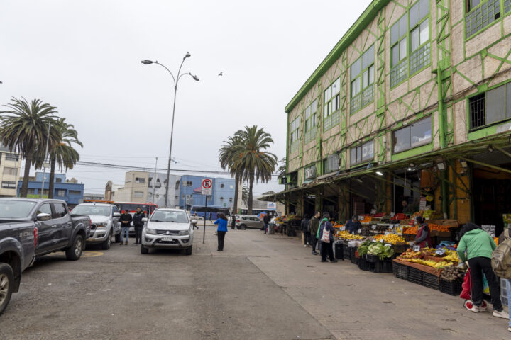 Vista del Mercado Cardonal en Valparaíso, mostrando varios vehículos aparcados y vendedores ofreciendo frutas y verduras en la acera.