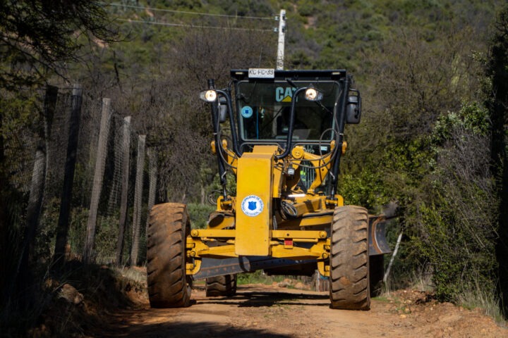 Motoniveladora amarilla de la Municipalidad de Quilpué en camino rural. Realiza conservación vial tras licitación fallida de Vialidad.