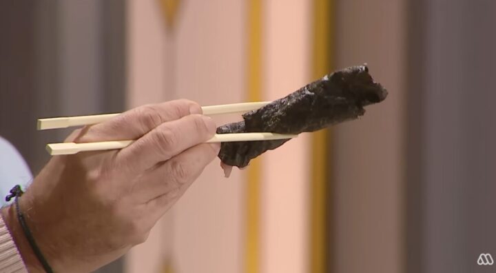 Mano con palillos sujetando un rollito de sushi de alga nori. Comida japonesa lista para degustar.