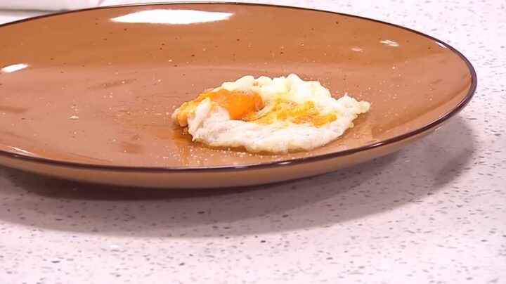 Huevo frito con yema naranja y clara cocida en plato marrón. Desayuno casero o comida rápida, sencillo y delicioso.