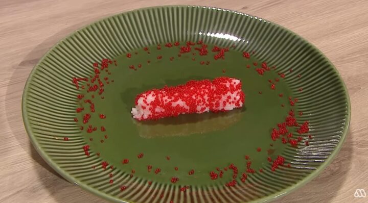 Rollo de sushi con huevas rojas vibrantes en plato verde estriado. Tobiko esparcido. Cocina japonesa, gourmet.