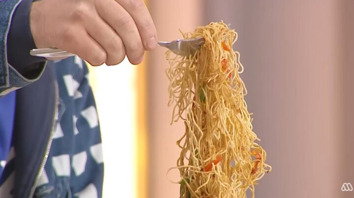 Mano con tenedor levanta fideos salteados con vegetales. Deliciosa pasta asiática lista para comer.